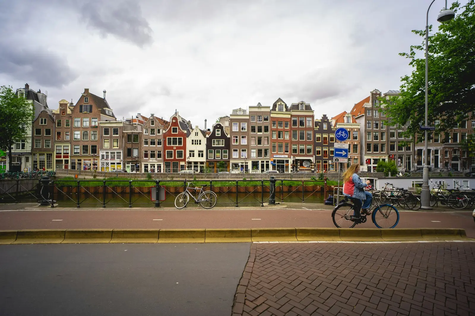 Een fietser op een gracht met bakstenen huizen erachter en klinkers op de stoep