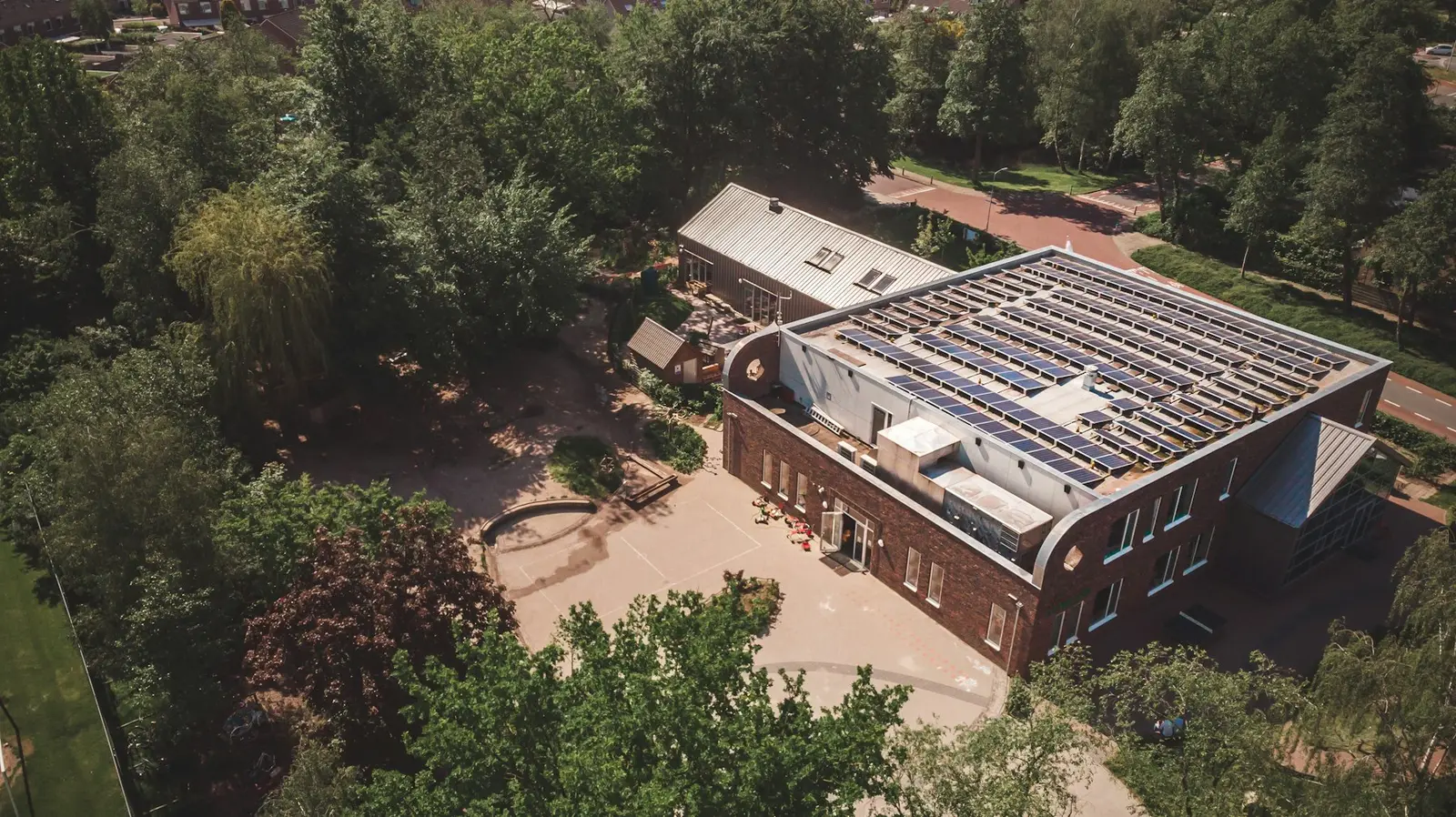 Een school met zonnepanelen op het platte dak tussen de bomen, van bovenaf gezien, in Nijkerk